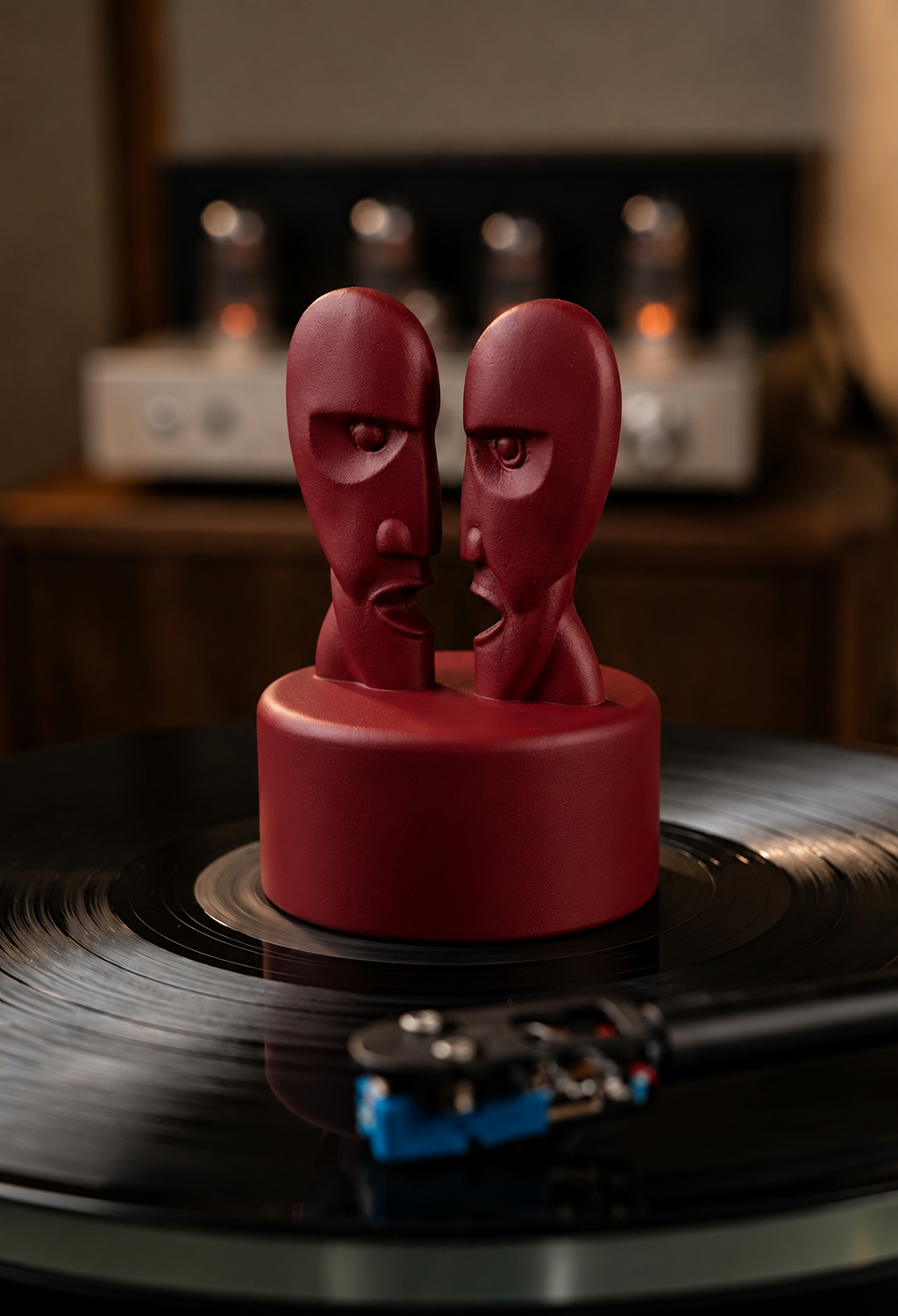 Dark red record stabilizer with dual face sculpture on a turntable.