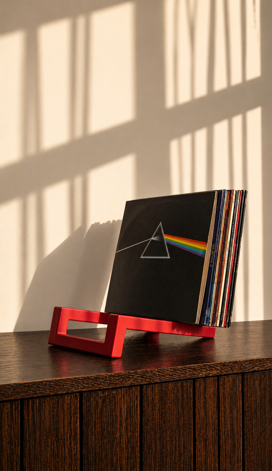 Red angular vinyl record stand holding a stack of albums on a wooden cabinet.