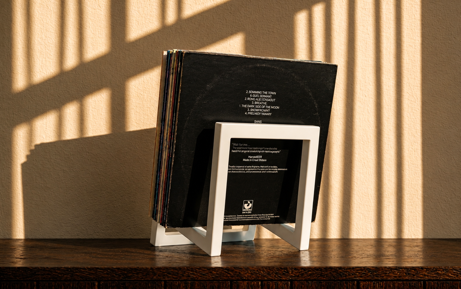 White square-frame vinyl record stand, back view, holding a stack of records.