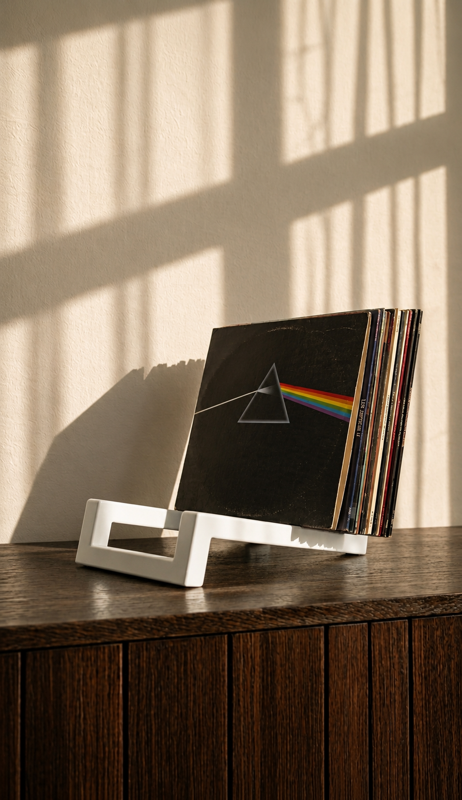 White angular vinyl record stand displaying a stack of albums on a wooden surface.