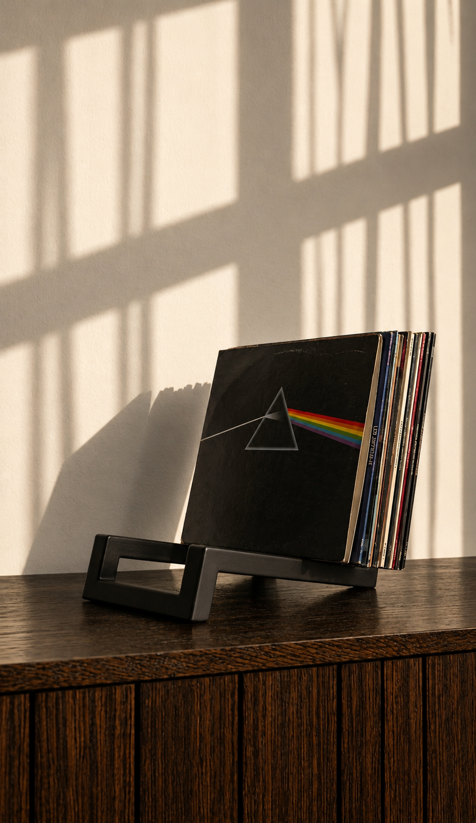 Black geometric vinyl record holder with a stack of albums on a wooden cabinet.