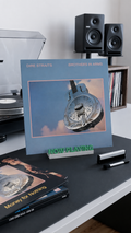 Green and white 'Now Playing' vinyl record stand holding an album on a desk.