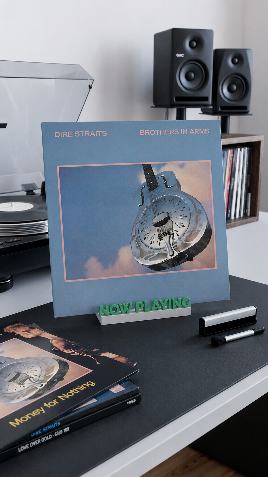 Green and white 'Now Playing' vinyl record stand holding an album on a desk.