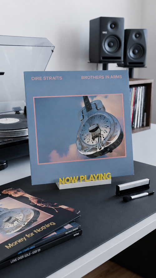 Yellow and white 'Now Playing' vinyl record stand holding an album on a desk.
