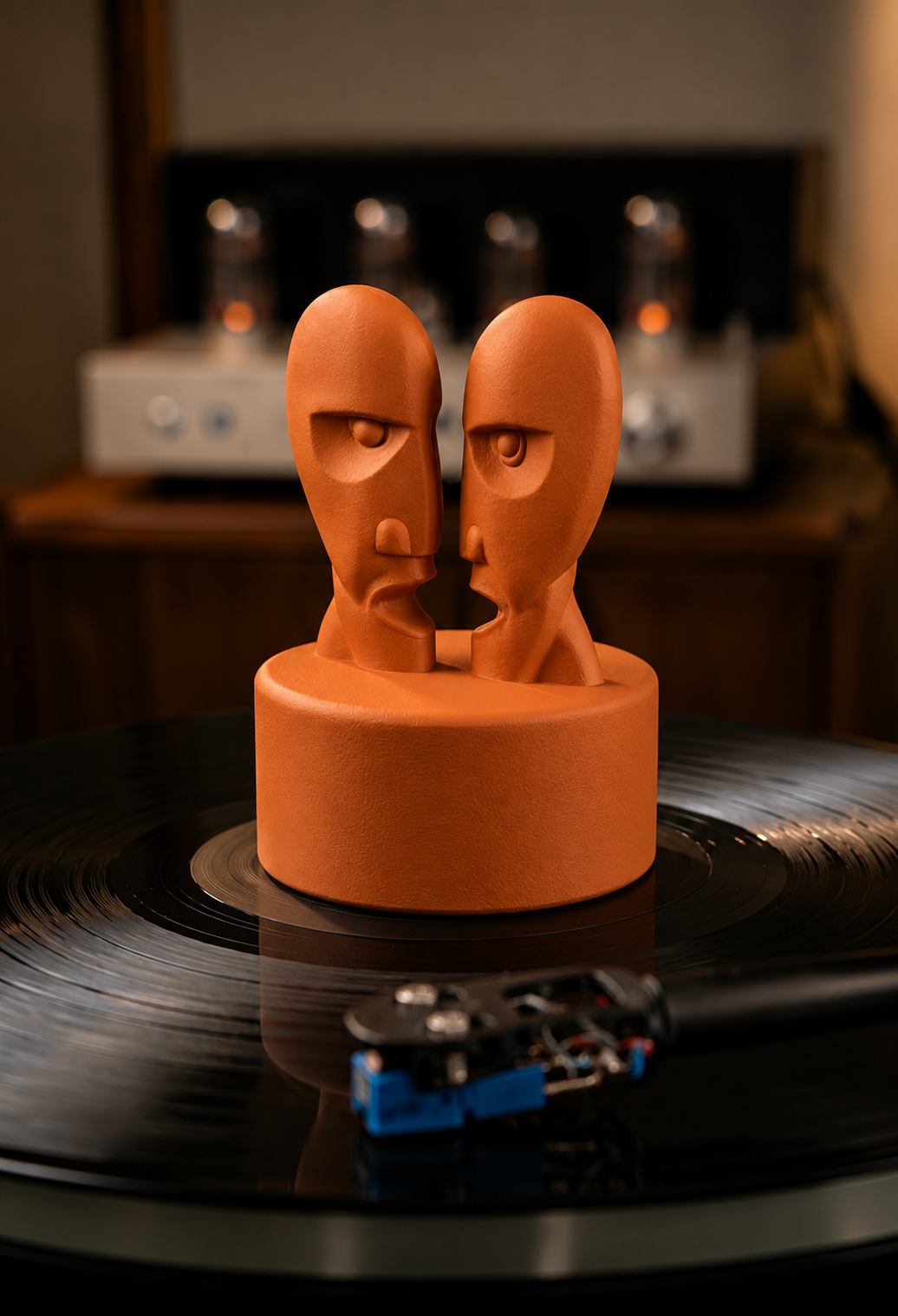Orange record stabilizer with sculpted faces on a turntable.