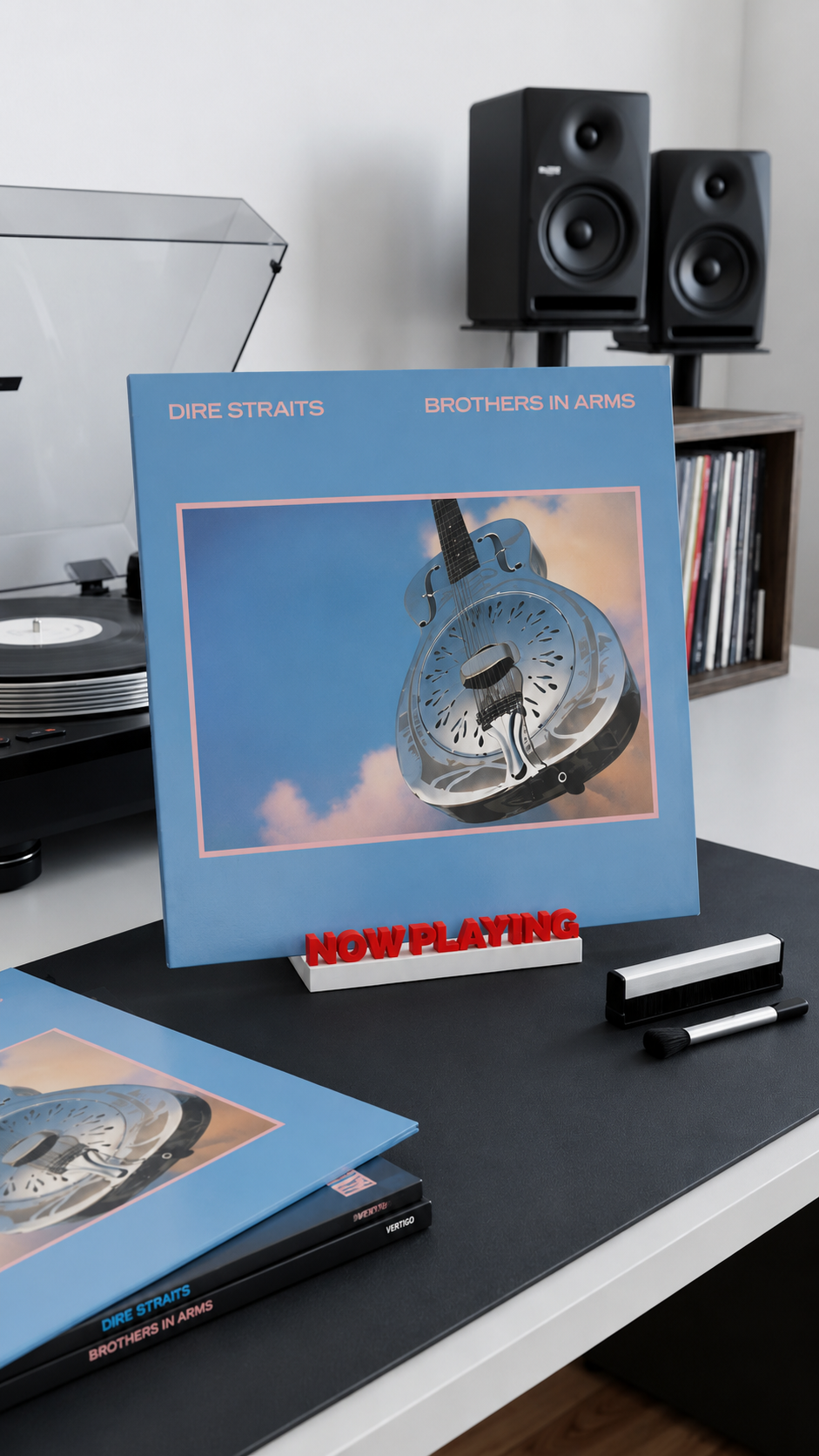 Red and white 'Now Playing' vinyl record stand holding an album on a desk.