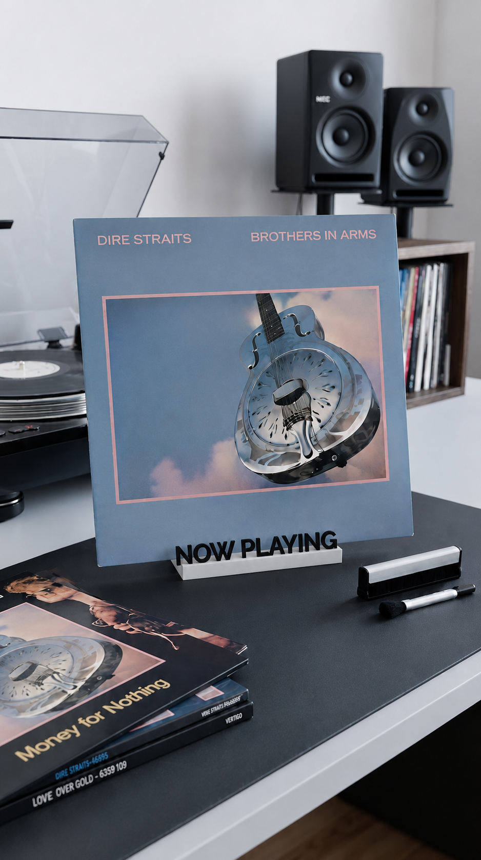 Black and white 'Now Playing' vinyl record stand holding an album on a desk.