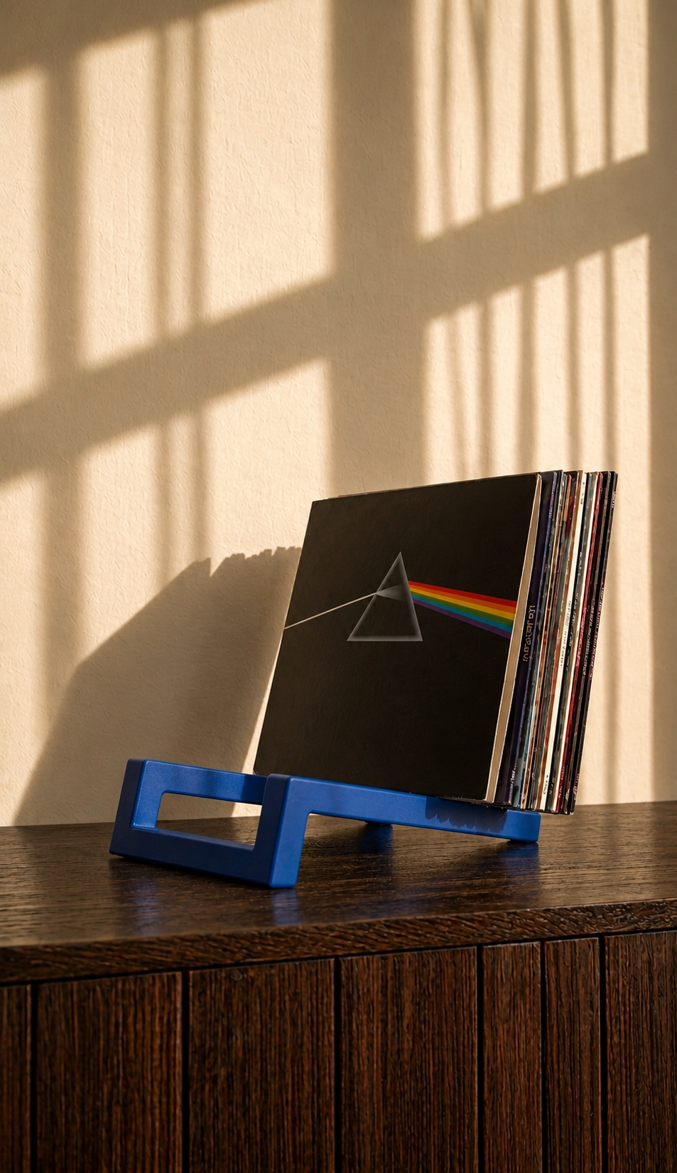 Blue angular vinyl record stand holding a stack of albums on a wooden cabinet.