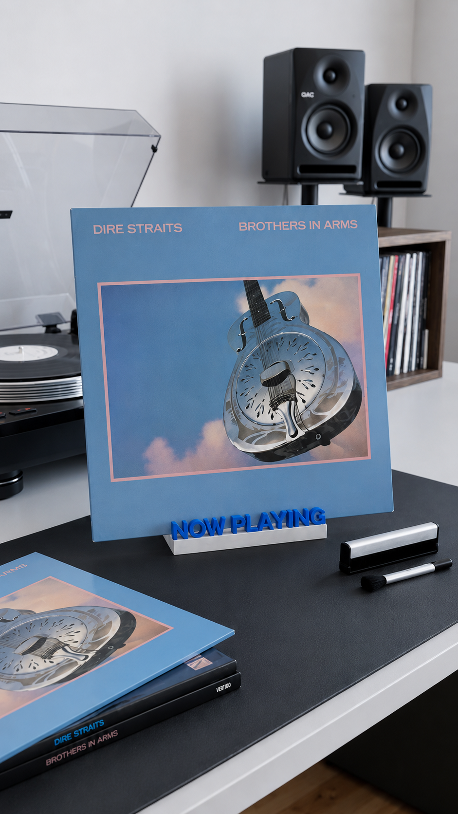 Blue and white 'Now Playing' vinyl record stand holding an album on a desk.